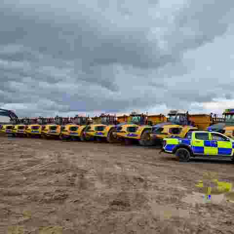 A police car parked to the right of a line of yellow off-road dumpers on a construction site.